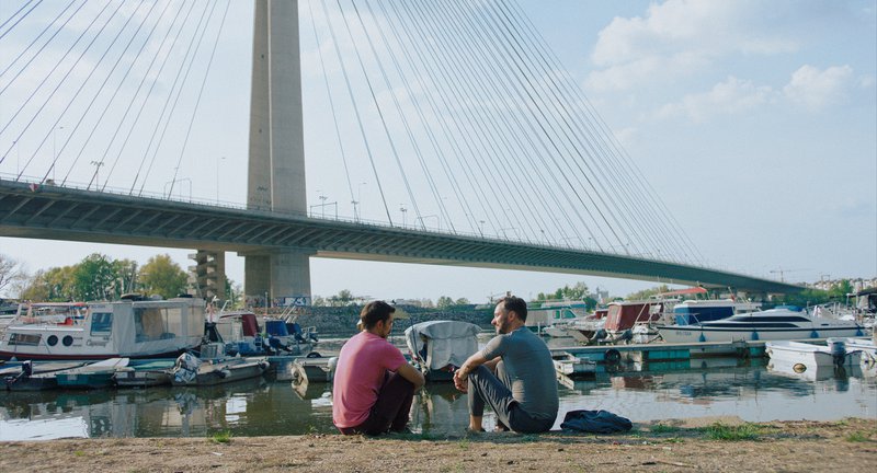 Zwei Menschen, die vor einem Fluss mit Booten sitzen